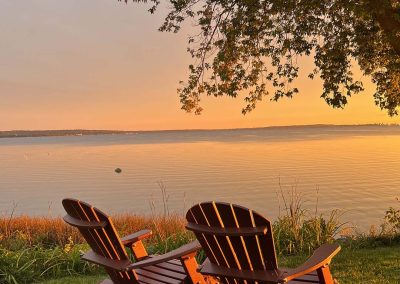 Portrait photo of two Adirondack chairs looking out over Lake Ontario just after sunset with golden hues; 2024 Photo Contest winner in the Landscape category, by Bridget Hughes
