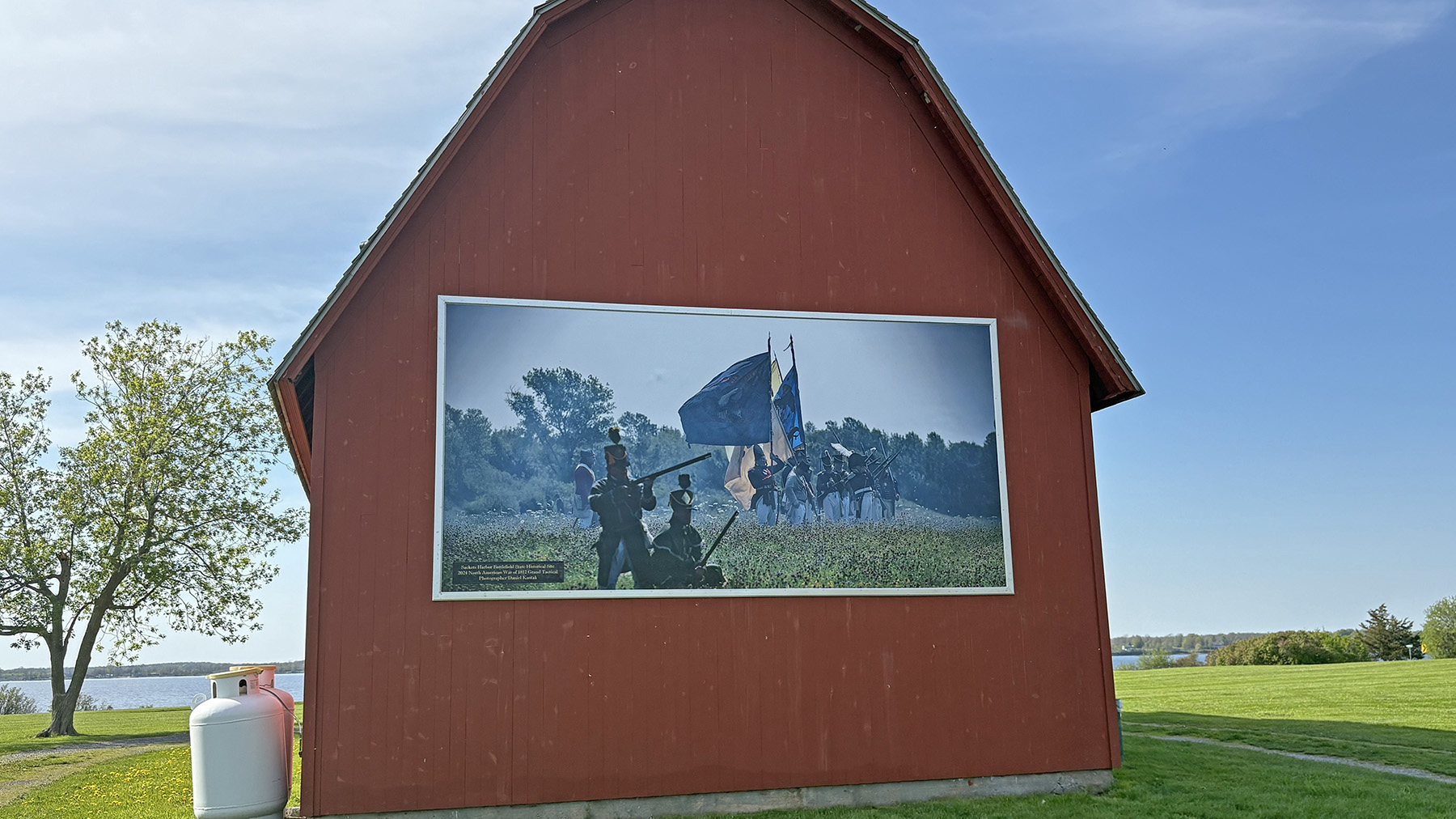 Photo of the Sackets Harbor Battlefield State Historic Site's red barn with a photo by Photographer and Poet Daniel Kantak