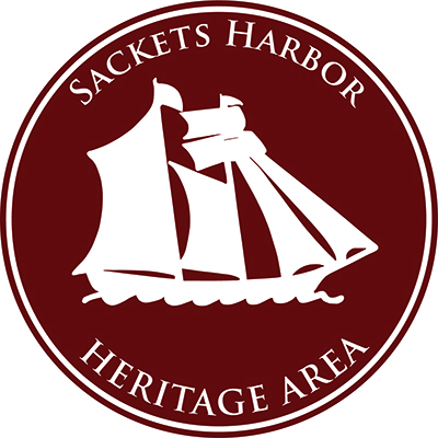 Full-color version of the Sackets Harbor Heritage Area logo, which depicts a white tall ship on a maroon background
