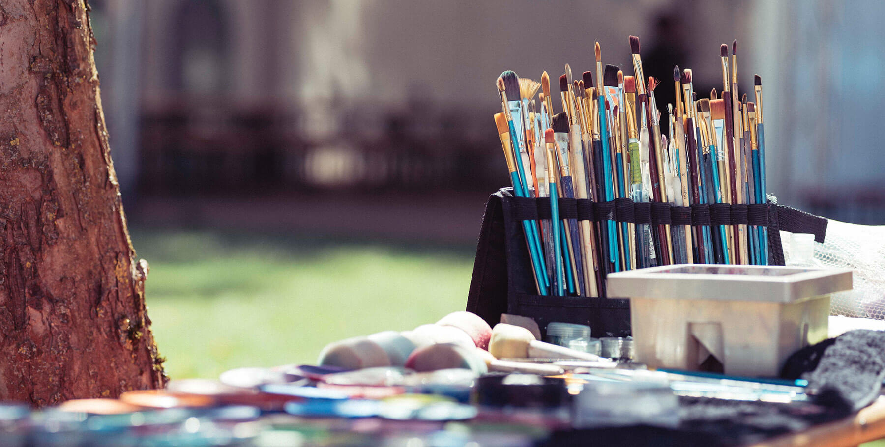 A large set of paint brushes and paints on a tray outdoors