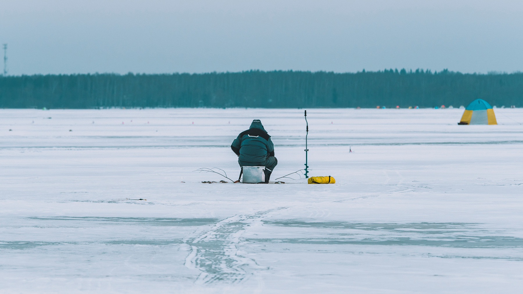 Color photo of a man fishing on a frozen lake (Image by Tom Grimbert for RawPixel.com)