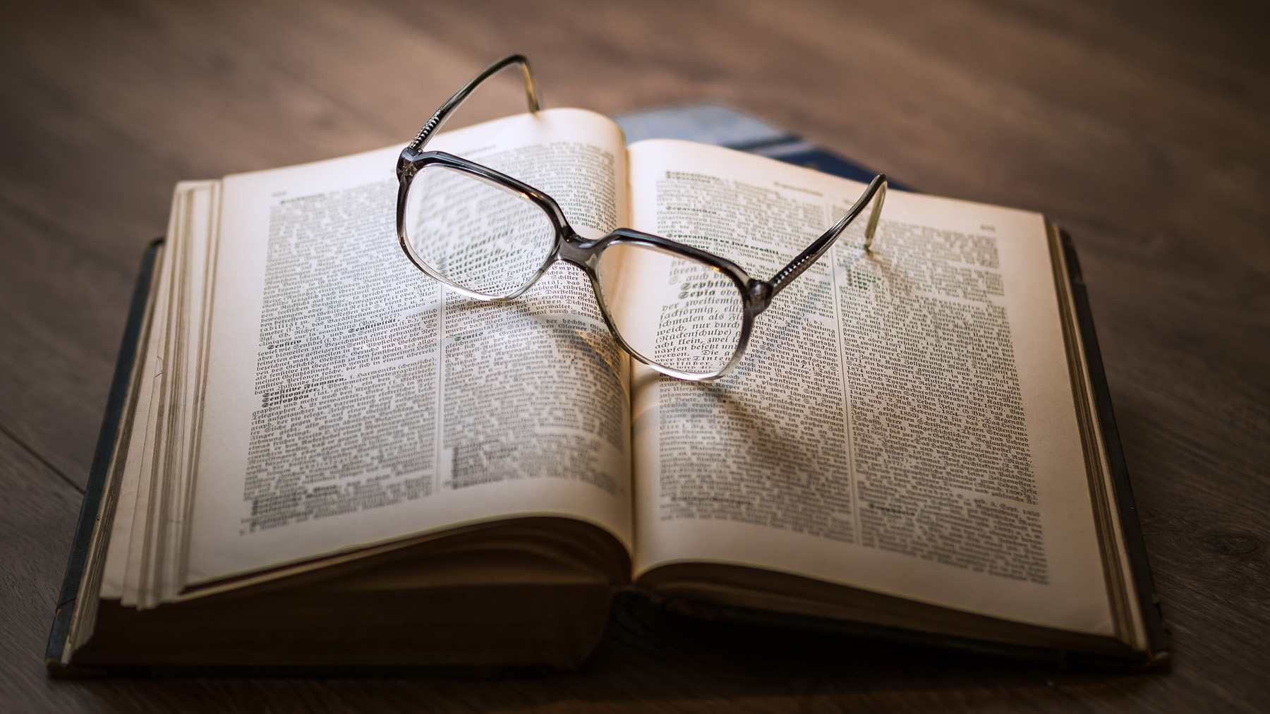 Color photo of eyeglasses sitting on top of an open book on a desk; Public domain photo, courtesy of RawPixel.com