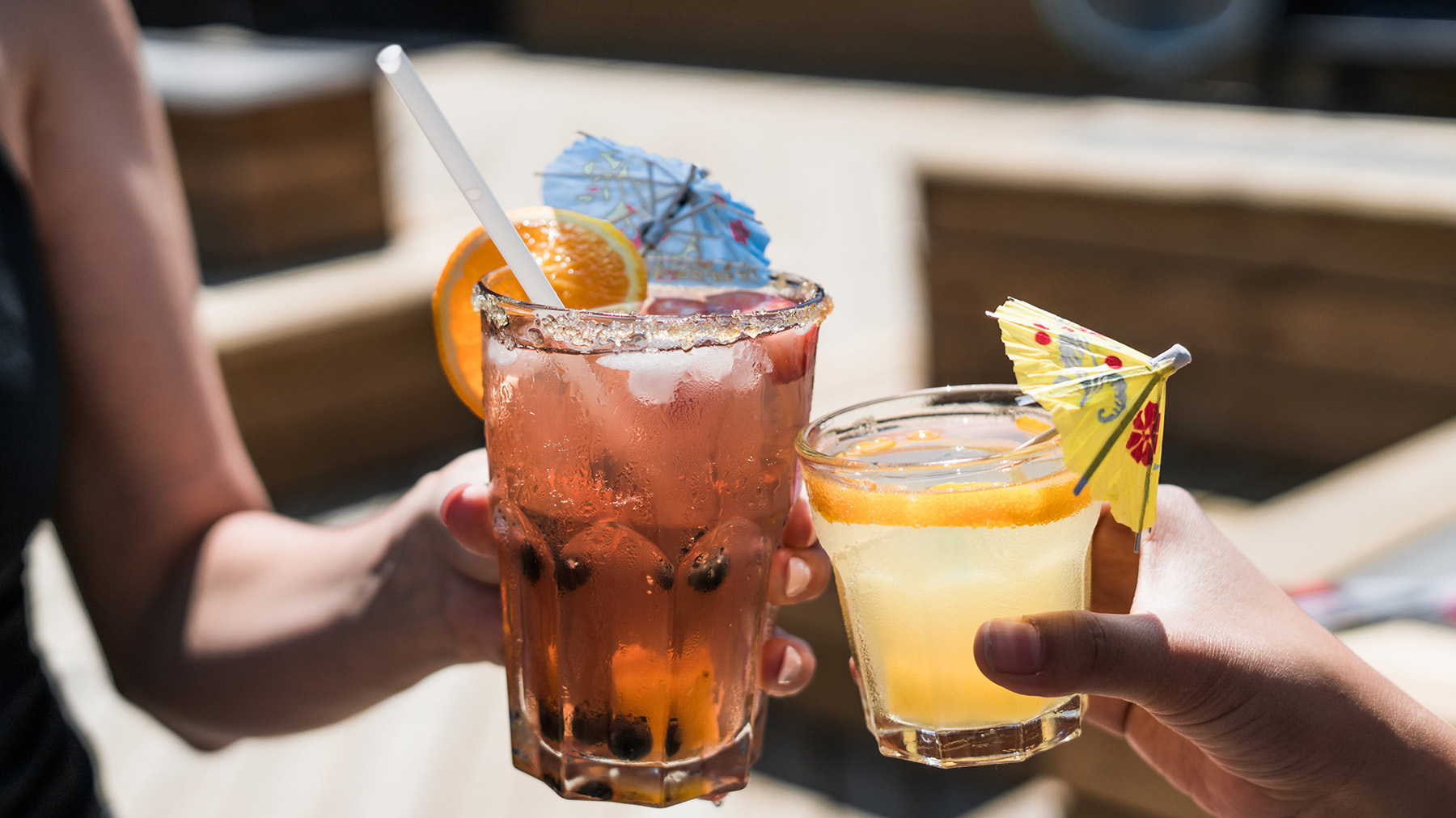 Color photo of two women's arms holding colorful, summer cocktails; Public domain image, courtesy of RawPixel.com
