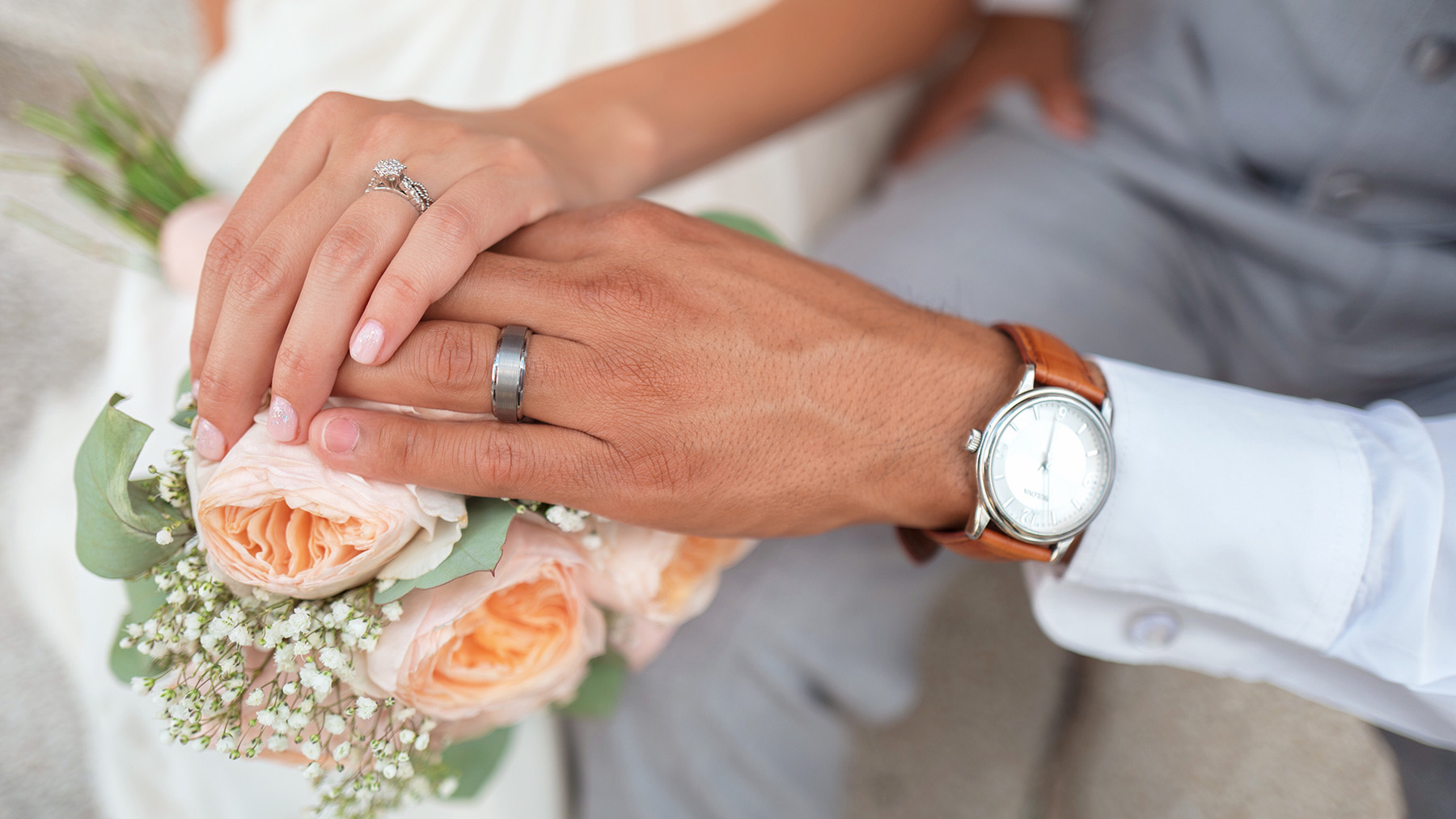 Color photo of a bride and groom's hands touching over a wedding bouquet; Public domain photo, courtesy of RawPixel.com